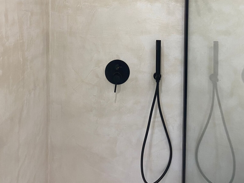Une douche à l'italienne réalisée avec du béton ciré et une robinetterie noire encastrée
