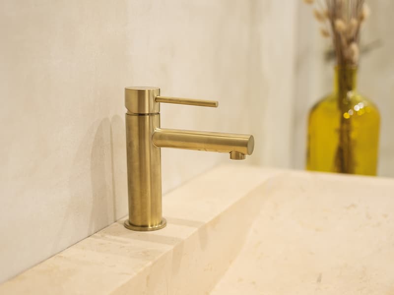 Une robinetterie dorée sur une vasque en travertin dans une salle de bain